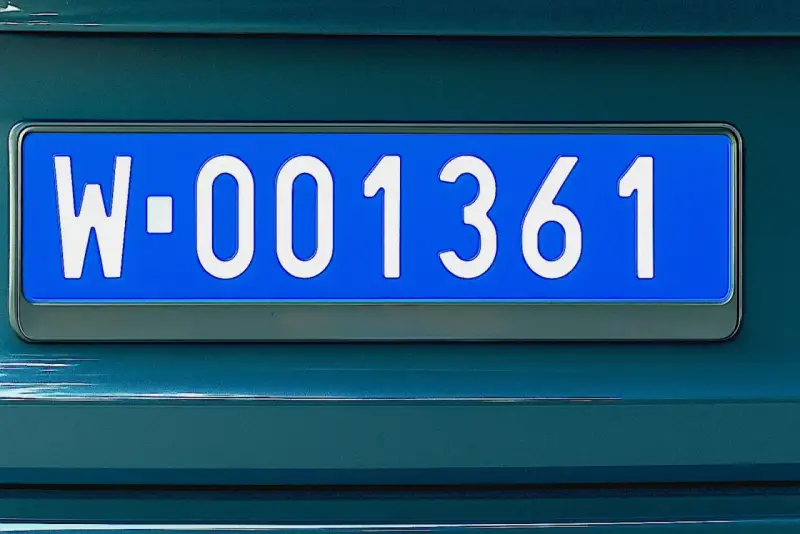 Niebieskie tablice rejestracyjne z numerem W-001361 na ciemnozielonym samochodzie.