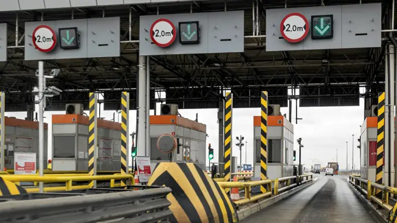 Bramki poboru opłat drogowych z tablicami informacyjnymi i zielonymi strzałkami wskazującymi przejazd.