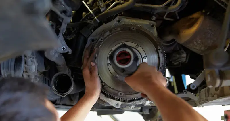 Mechanik dokonuje wymiany dwumasy w samochodzie, pracując przy skrzyni biegów.