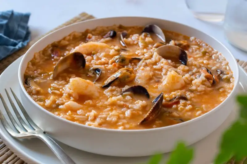 Un delicioso arroz caldoso de marisco, repleto de gambas, mejillones y almejas, servido en un cuenco blanco.