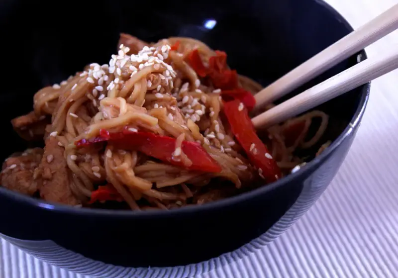 Miseczka pełna aromatycznego makaronu teriyaki z kawałkami kurczaka i papryką, posypana sezamem.