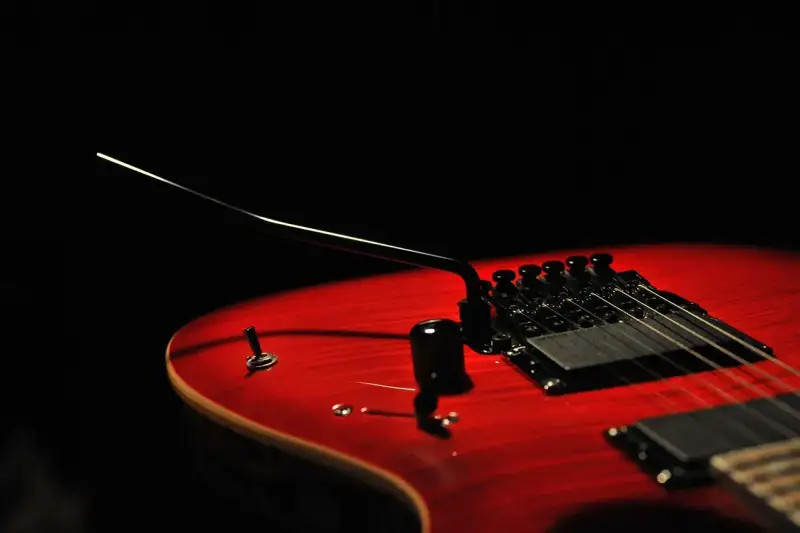 Czerwona gitara elektryczna z czarnym mostkiem tremolo, gotowa do wydobycia dźwięków, które poruszą serce.