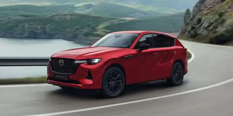 Czerwona Mazda CX-60 3.3 Diesel pokonuje zakręt na malowniczej drodze.