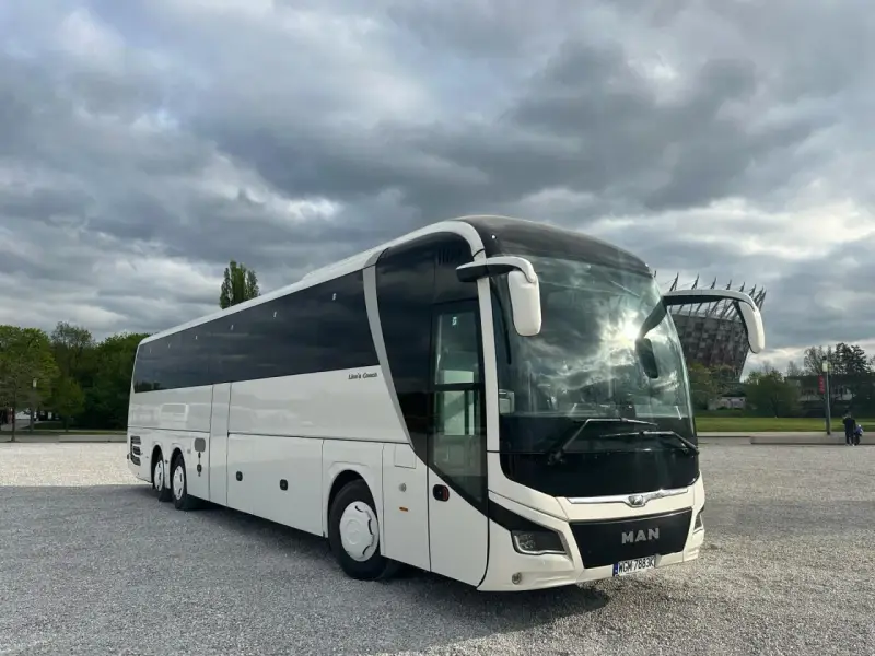 Biały MAN Lion's Coach, nowoczesny autokar turystyczny, zaparkowany na żwirowym placu pod pochmurnym niebem.
