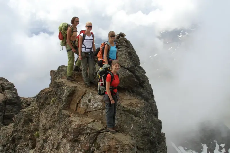 Quattro escursionisti con zaini si fermano sulla cima rocciosa di Cima Sternai, circondati da nuvole e nebbia.