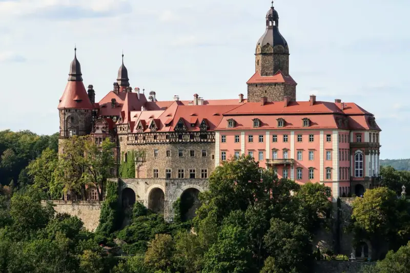 Zamek Książ z czerwonymi dachami i wieżami, otoczony zielenią. Sprawdź zamek książ cennik zwiedzania.