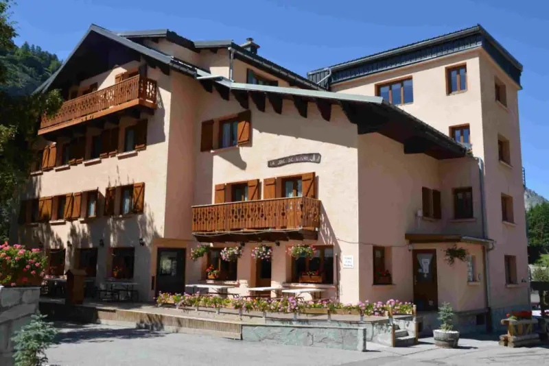 Bâtiment de style alpin avec balcons en bois et volets marrons, fleuri. Une enseigne "La Joie de Vivre" suggère une ambiance de colonie en Haute-Savoie.