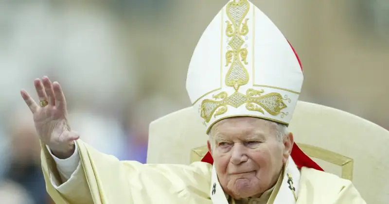 Papież Jan Paweł II w białej mitrze z haftem, pozdrawia wiernych. Jego dłoń z pierścieniem jest uniesiona. Codzienna modlitwa do św. Jana Pawła II.