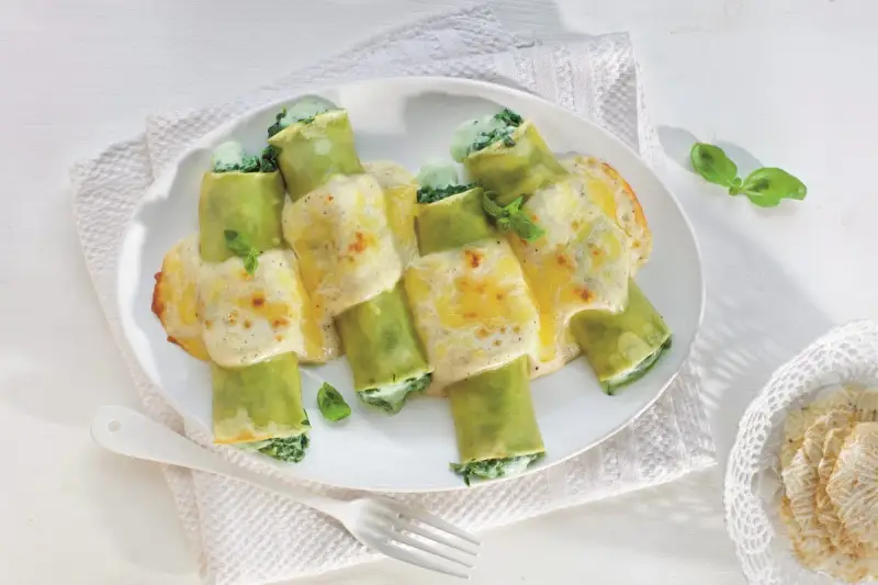 Zielone cannelloni ze szpinakiem, zapieczone pod kremowym sosem serowym, ozdobione listkami bazylii.