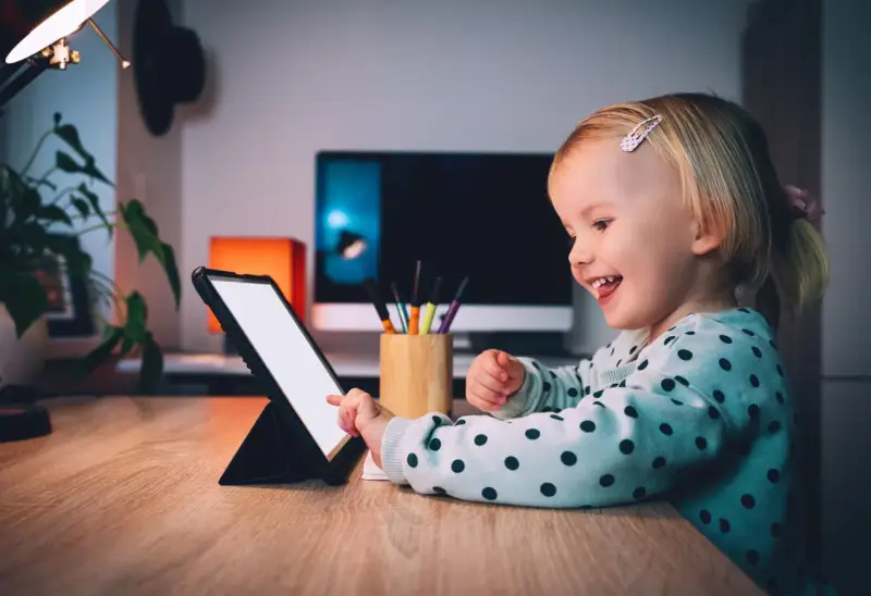 Uśmiechnięta dziewczynka ogląda ulubionych youtuberów dla dzieci na tablecie.