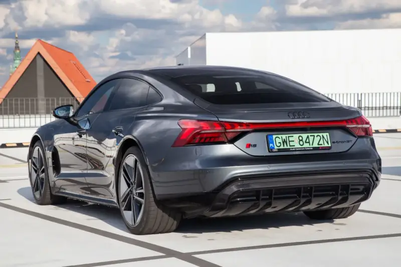 Tył ciemnoszarego Audi RS e-tron GT na parkingu, z widocznymi światłami i tablicą rejestracyjną.
