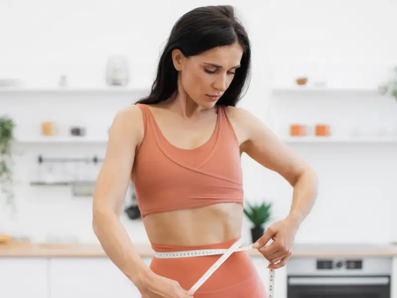Kobieta w sportowym stroju mierzy talię, ciesząc się efektami diety low carb.