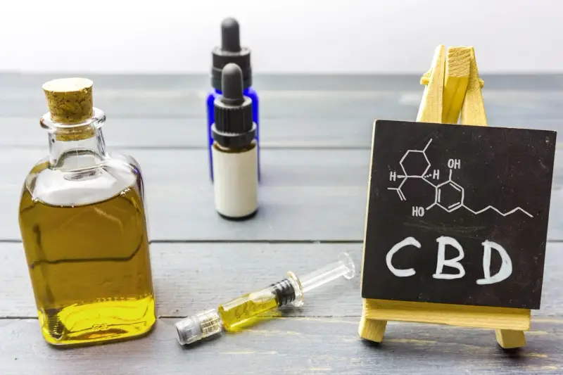 Butelka z olejkiem, strzykawka i tabliczka z napisem CBD. Zastanawiasz się, olejek CBD na co?