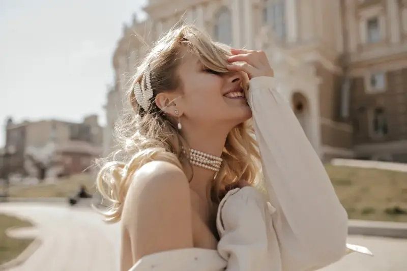 Uśmiechnięta blondynka w perłowej biżuterii, z perłową spinką we włosach. Masa perłowa znaczenie symbolizuje czystość i piękno.