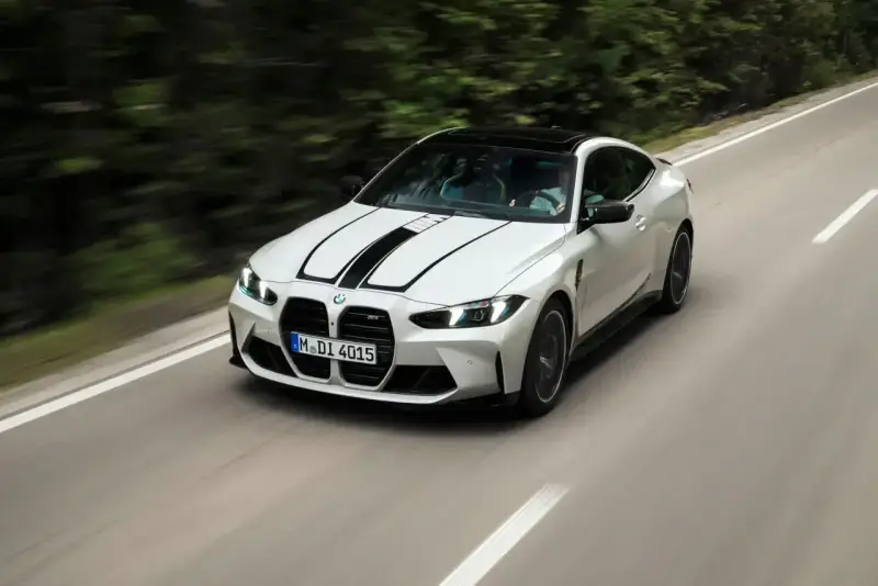 Białe BMW M4 z czarnymi pasami na masce pędzi po krętej drodze. Zastanawiasz się, ile kosztuje BMW M4?