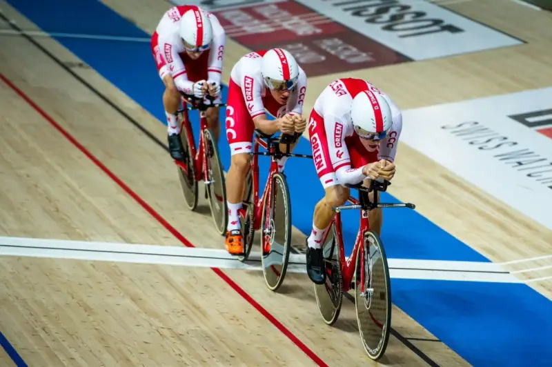 Trzech kolarzy w biało-czerwonych strojach ściga się na welodromie. Ich rowery i stroje mają logo ORLEN. To dynamiczne keirin kolarstwo.