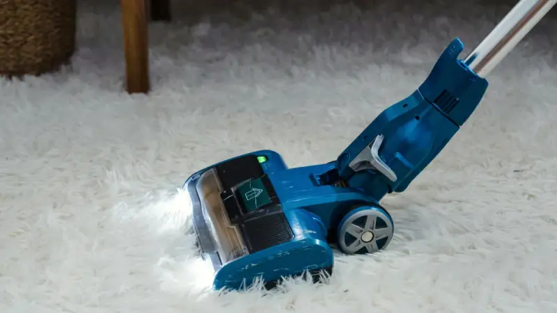 Blauer Staubsauger mit LED-Licht reinigt flauschigen Teppich. Die Leistung, wie viel Watt hat ein Staubsauger, ist entscheidend für die Saugkraft.
