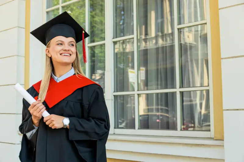 Uśmiechnięta absolwentka z dyplomem, w todze i birecie, zastanawia się, co to studia MBA i jakie możliwości otwierają.