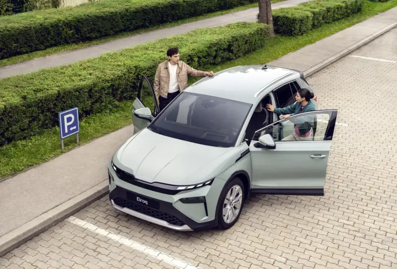 Jasnoszary elektryczny SUV Škoda Elroq z otwartymi drzwiami, obok którego stoją młoda kobieta i mężczyzna.
