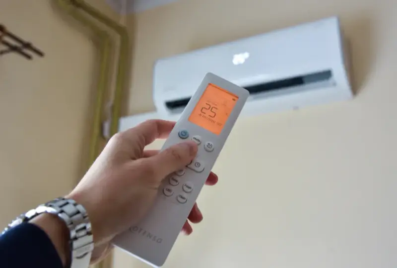 Dłoń trzymająca pilot do klimatyzacji, ustawiona na 25°C. Kontroluj komfort i miesięczny koszt klimatyzacji.