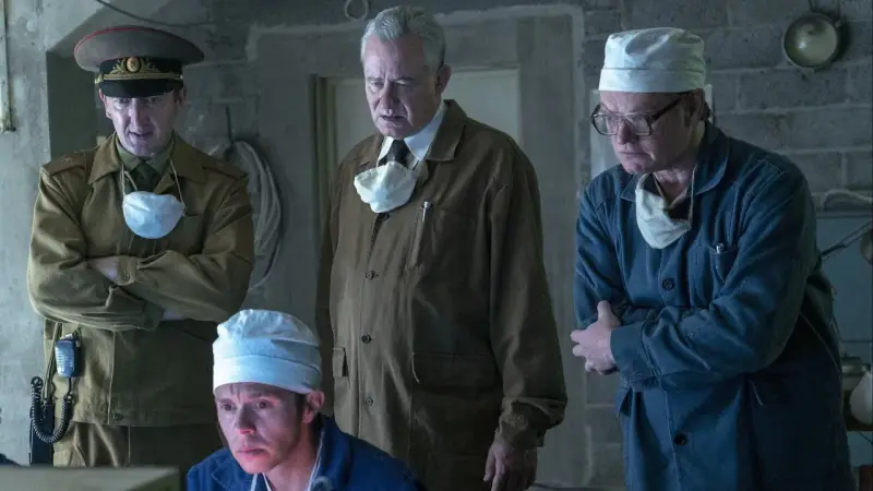 Mężczyźni w mundurach i fartuchach, w tym jeden w wojskowym, analizują coś na ekranie. Scena z serialu Czarnobyl Netflix.