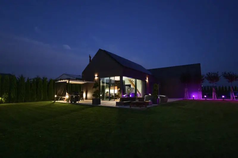 Nowoczesny dom nocą, z oświetlonym ogrodem i tarasem. Analiza prawdziwych kosztów eksploatacji domów pasywnych w polskich warunkach klimatycznych.