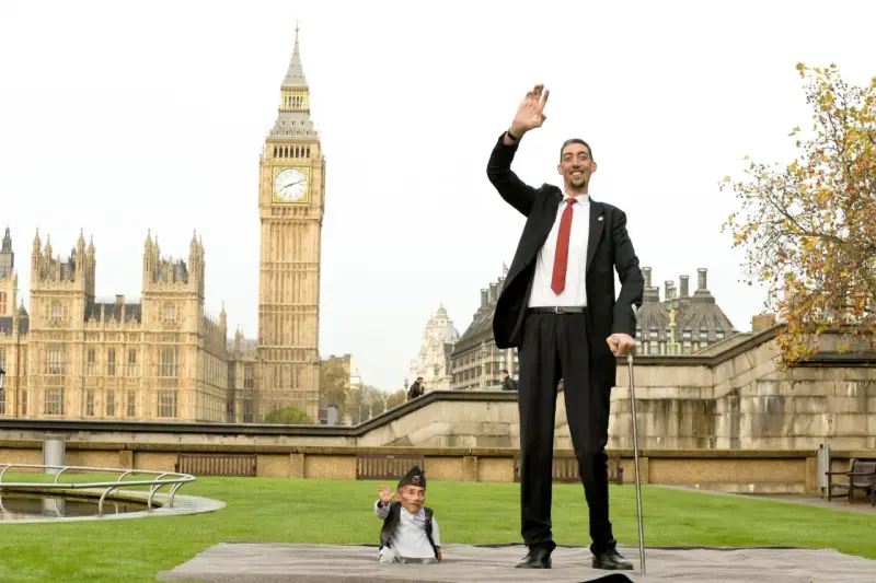 Der größte Mensch der Welt winkt vor dem Big Ben in London. Neben ihm steht ein Mann von sehr kleinem Wuchs.