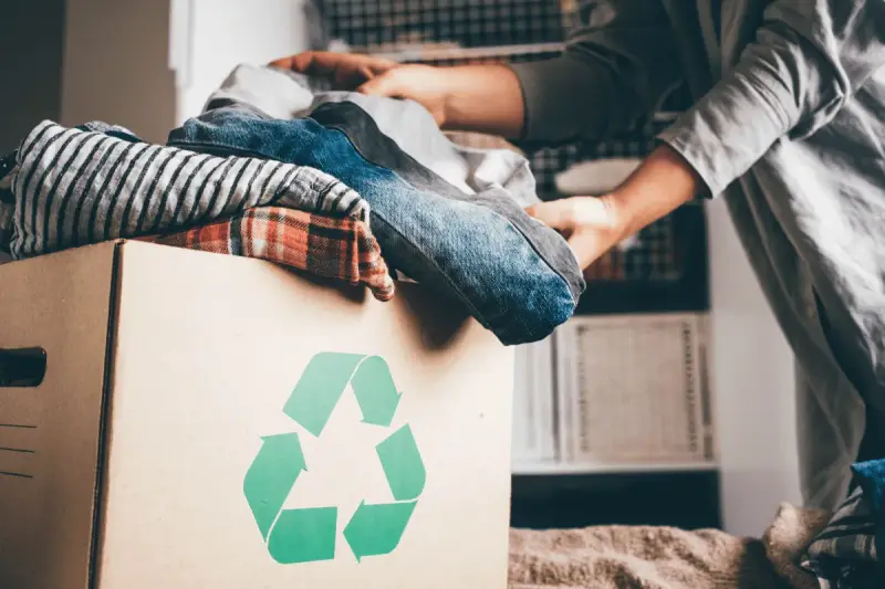 Pudełko z ubraniami i symbolem recyklingu. Wiesz, gdzie można oddać ubrania za darmo?