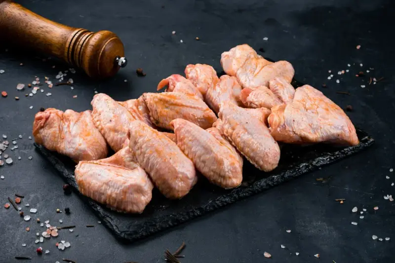 Skrzydełka kurczaka gotowe do pieczenia, zamarynowane w aromatycznej solance. Obok młynek do pieprzu i gruboziarnista sól.
