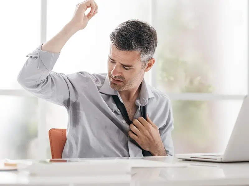 Uomo d'affari con camicia bagnata di sudore sotto le ascelle, che si sbottona la cravatta. Le cause del sudare freddo sono molteplici.