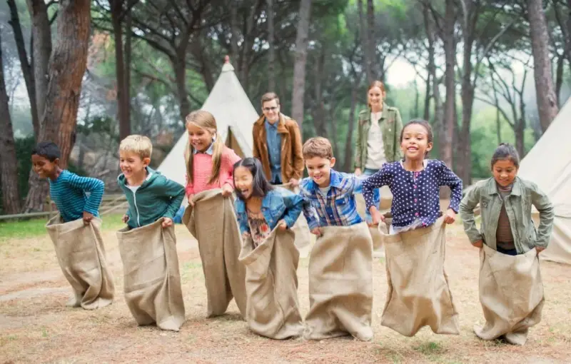 Des enfants participent à une course en sac dans un camp de vacances en forêt.