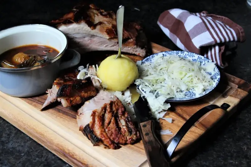 Deftige dicke Rippe mit Klößen, Sauerkraut und dunkler Soße auf Holzbrett.