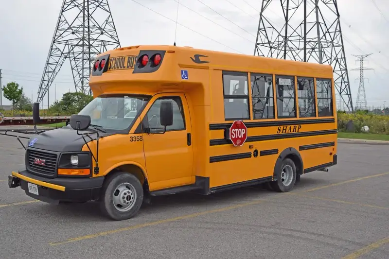Żółty autobus szkolny GMC z napisem "SHARP" i znakiem STOP. Zastanawiasz się, ile kosztuje autobus?
