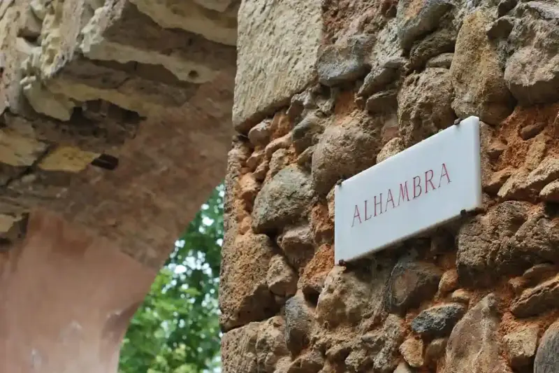 Schild "Alhambra" an einer alten Steinmauer, die zu einem Parkplatz führt.