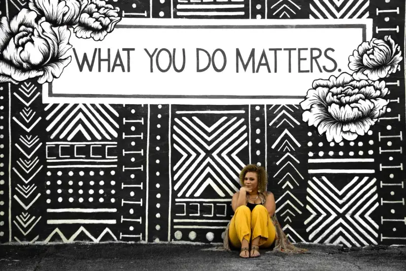 Kobieta siedzi przed muralem z napisem "WHAT YOU DO MATTERS". To inspirujący dialog motywujący.