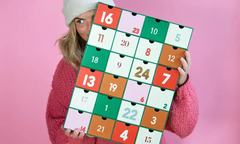 En person med en stickad tröja och mössa håller upp en färgglad julkalender. En perfekt julkalender diy att skapa själv!