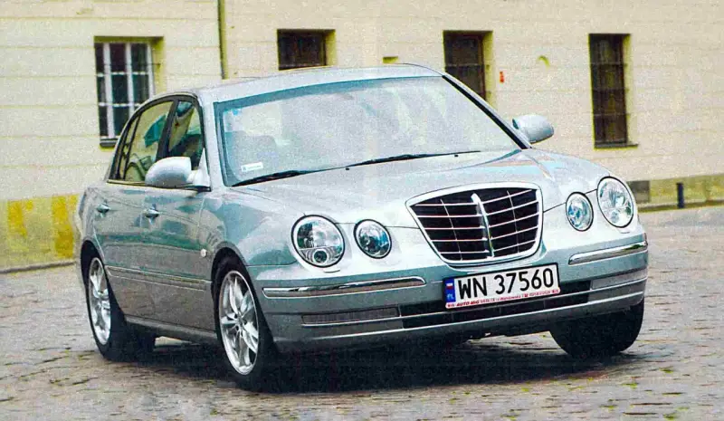 Srebrny Kia Opirus z polskimi tablicami rejestracyjnymi WN 37560 na brukowanej ulicy.
