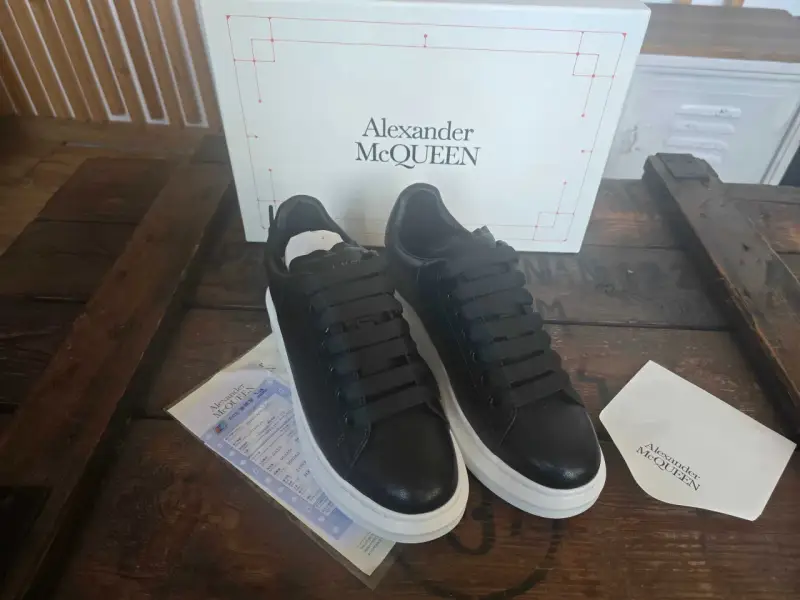 Czarne sneakersy Alexander McQueen na grubej, białej podeszwie, obok pudełka z logo marki.