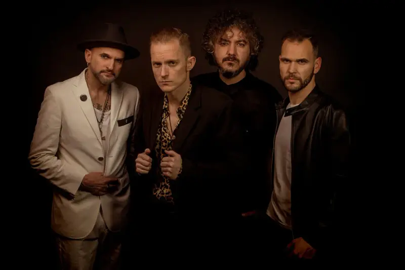 El grupo de embusteros posa con miradas intensas. Uno lleva sombrero y traje blanco, otro camisa de leopardo, y los otros dos, chaquetas oscuras.