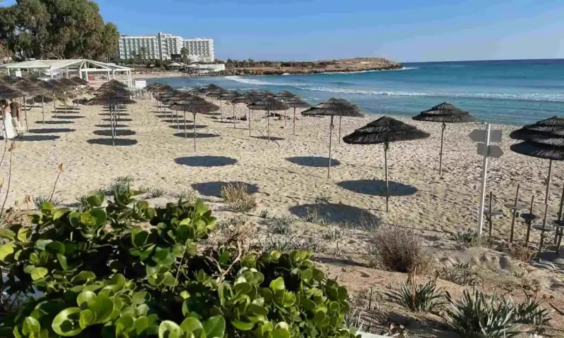 Puste cypr plaże z rzędami parasoli i hotel w tle. Słońce rzuca długie cienie na piasek.