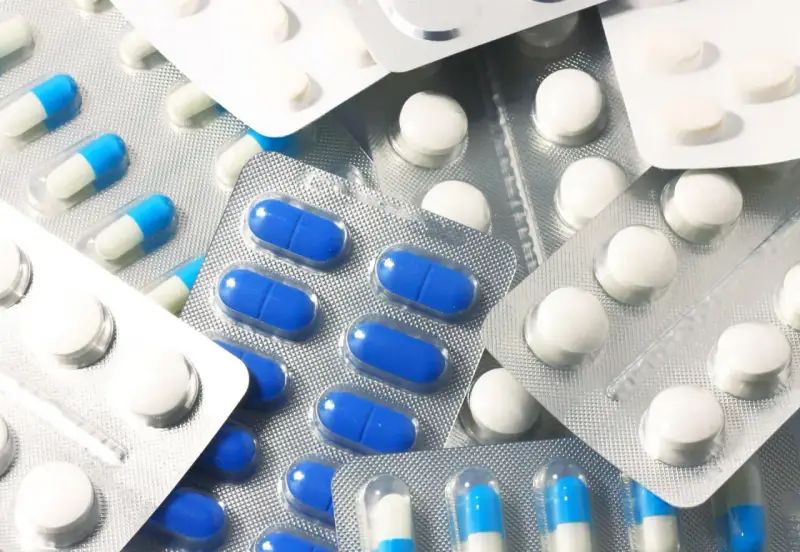 Blistry z białymi i niebiesko-białymi kapsułkami oraz białe tabletki. Wśród nich można znaleźć polopirynę, która pomaga złagodzić ból i gorączkę.