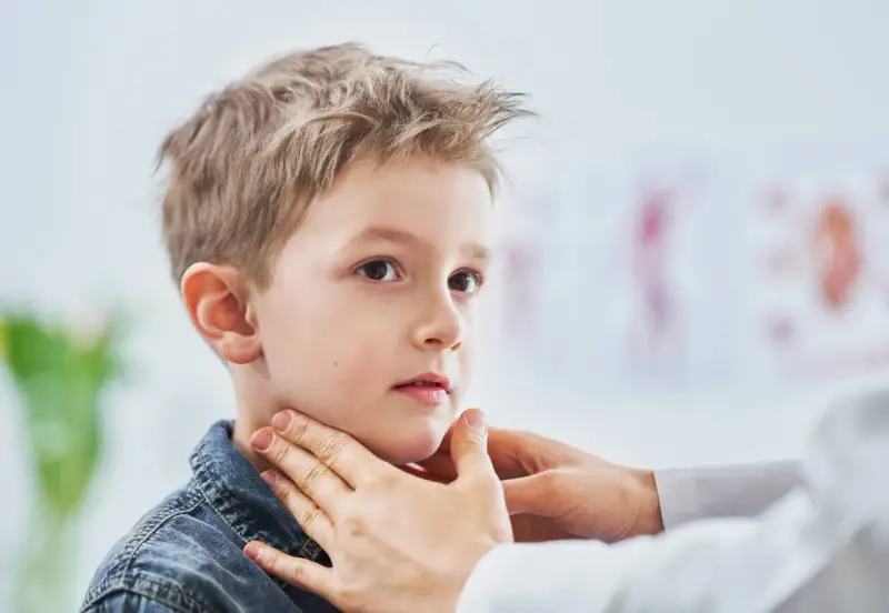 Lekarz bada szyję chłopca, sprawdzając, czy nie ma powiększonych węzłów chłonnych u dzieci. Zdjęcia takie pokazują ważny element diagnostyki.