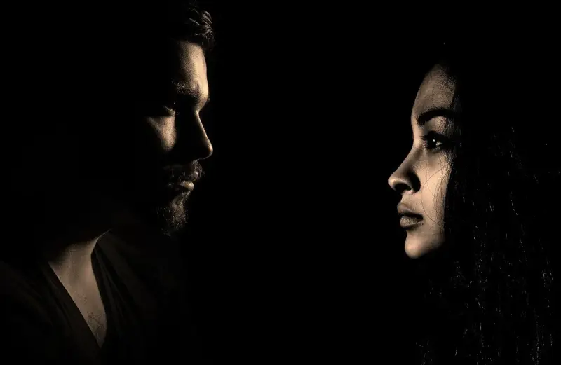 Mężczyzna i kobieta patrzą na siebie w mroku. Ich profile, oświetlone z boku, sugerują napięcie i tajemnicę, jak w grach czarnej psychologii.
