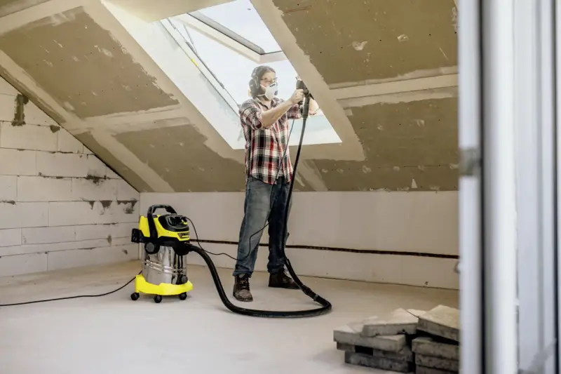 Man med skyddsutrustning använder Kärcher WD 6 för att dammsuga vid renovering av ett vindsrum.
