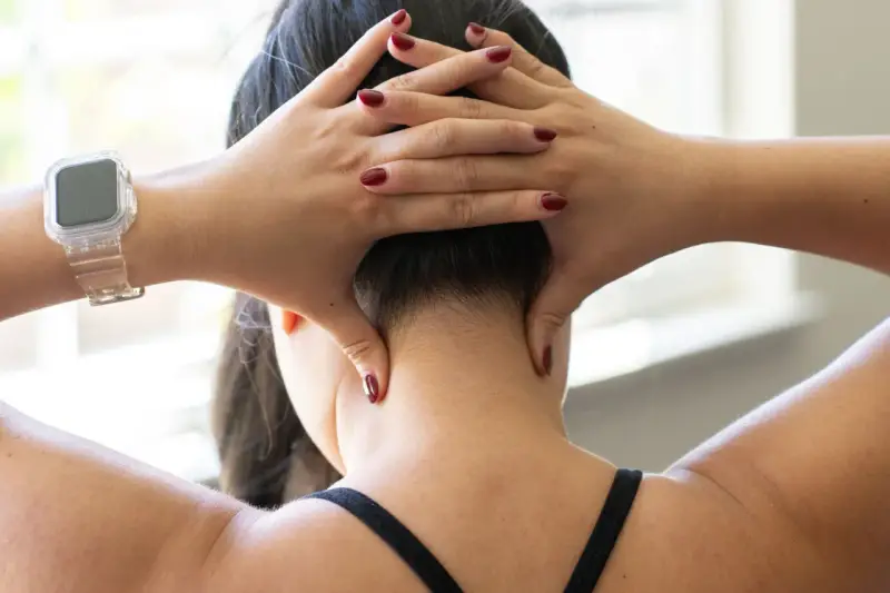 Hands demonstrate shiatsu self neck massage techniques, applying pressure to the base of the skull and sides of the neck.