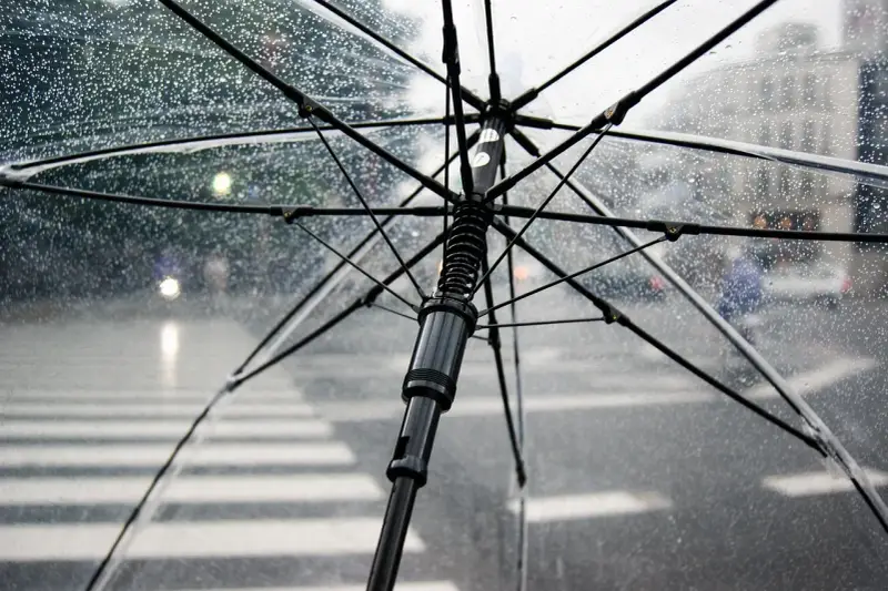 Przezroczysty parasol w bagażu podręcznym chroni przed deszczem na ulicy. Krople wody na materiale.