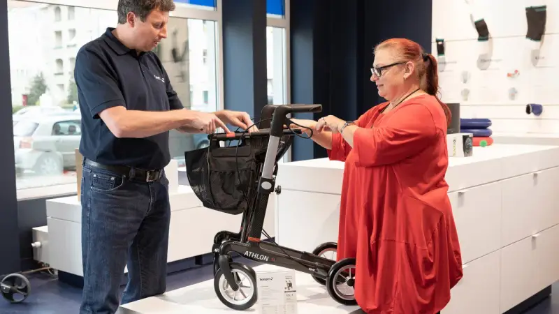 Mann erklärt einer Frau einen Rollator, ein wichtiges medizinisches Hilfsmittel, im Sanitätshaus.
