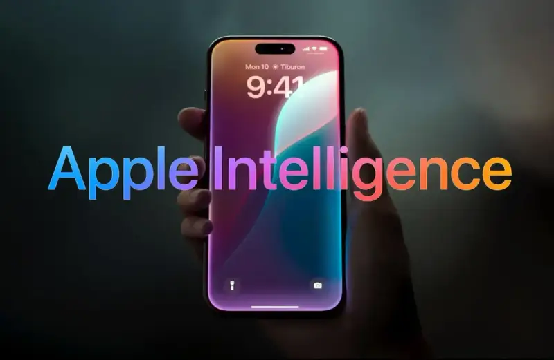 Dłoń trzyma smartfon z ekranem blokady, na którym widnieje napis "Apple Intelligence" w tęczowych barwach.
