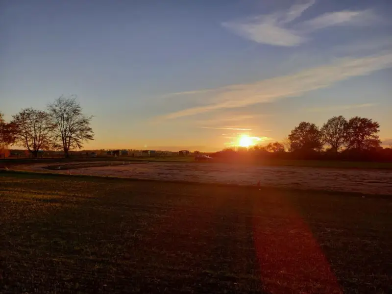 Sonnenuntergang über einem Feld mit Bäumen und einem Auto. "Seid stille und wisset: Ich bin Gott." (Psalm 46:10)