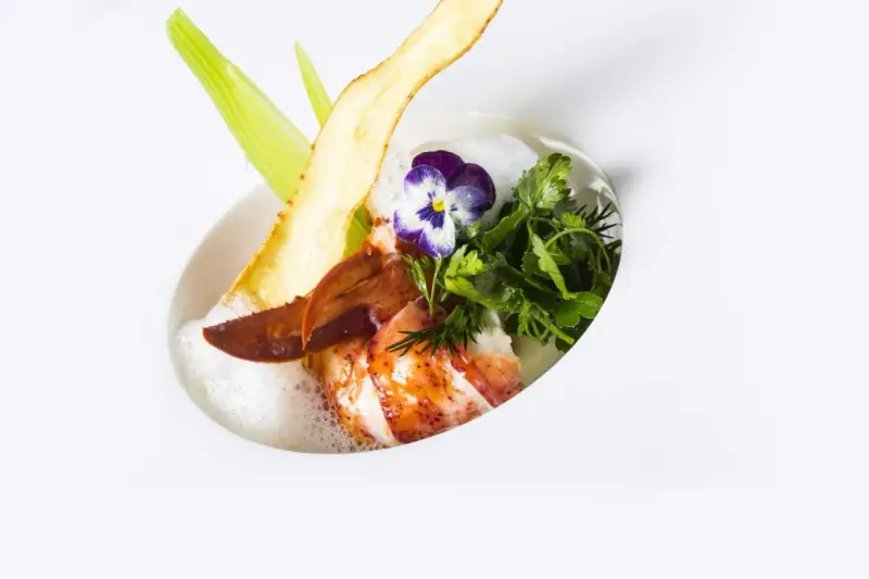 Homard poêlé, écume légère, chips de légume et fleur, une spécialité jurassienne raffinée.